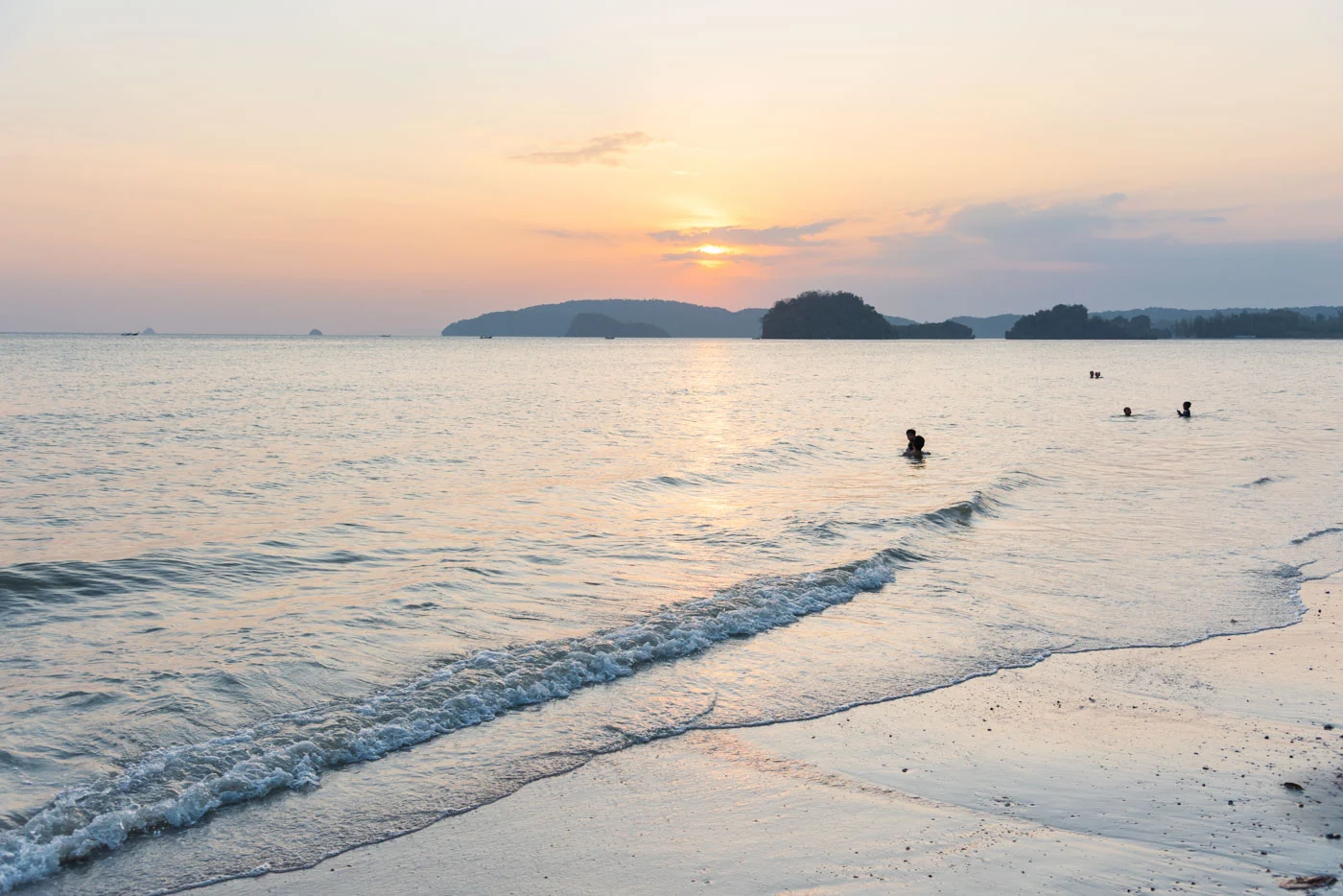 Coucher de soleil sur la plage de Nopparat Thara avec silhouettes de baigneurs dans l'eau